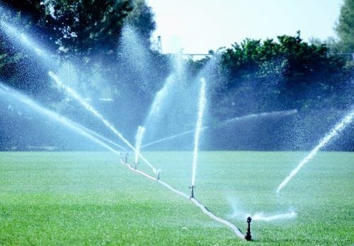 Irrigation sprinklers spraying an even arc of water across a bright green lawn