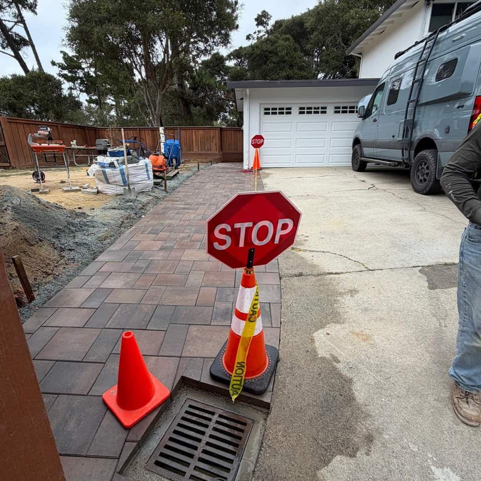 New paver driveway with a drain grate in front of a garage during installation